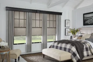 Window Treatments 10 Elegant bedroom showcasing layered window treatments with light gray drapes and textured roller shades, framed by white walls and a vaulted ceiling.