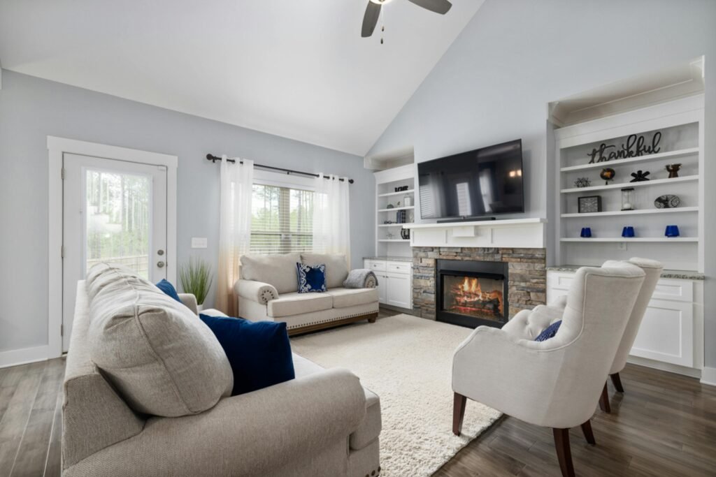 interior-furniture-decor-styling-4 Cozy and stylish living room featuring neutral-toned furniture with navy accent pillows, a stone fireplace with a mounted TV, and built-in white shelving. Light blue walls and wood flooring complement the bright and inviting decor, creating a balanced and elegant furniture styling setup. Perfect example of thoughtful interior design and home décor styling.
