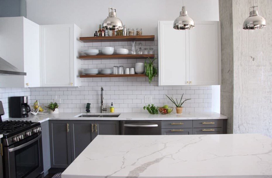 Modern kitchen with white upper and gray lower cabinets, marble‑veined quartz countertops, open wood shelving, subway tile backsplash, stainless‑steel range and sink, and chrome pendant lights.