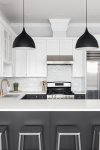Kitchen Design 10 Modern kitchen with white upper cabinets and dark gray lower cabinets, paired with stainless steel appliances. A large island with white countertops and metal barstools sits under two black pendant lights, creating a sleek contrast.