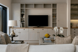Interior & Exterior Paint Consultations 4 Modern living room with built-in cabinetry and shelving framing a flat-screen TV. Neutral tones, wood accents, and decorative objects like books, plants, and orchids create a balanced and inviting design.
