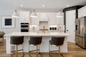 Kitchen Design 13 Minimalist kitchen with light gray cabinetry and a large island topped with a polished marble countertop. Pendant lights with smoky glass shades add warmth, while wood stools and stainless steel appliances complete the clean, modern look.