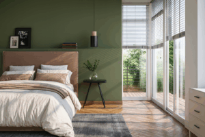 Interior & Exterior Paint Consultations 5 Contemporary bedroom with a green accent wall, wood flooring, and floor-to-ceiling windows that open to a balcony view of trees. The space features a warm-toned upholstered headboard, neutral bedding, and a small black side table.