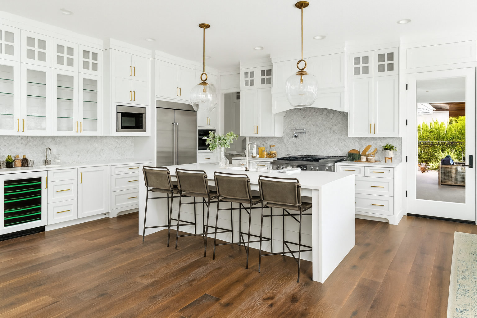 Bright farmhouse-style kitchen with white cabinets, marble backsplash, and a large center island. The design includes brass hardware, glass pendant lights, and wide-plank wood flooring for a blend of elegance and comfort.