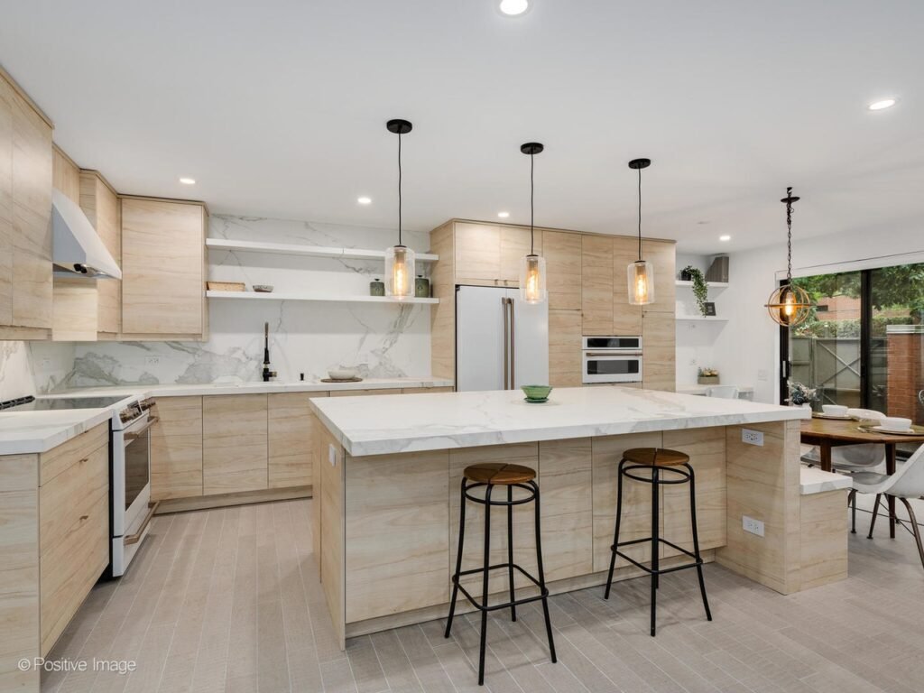 kitchen-remodel-southloop-chicago-il Modern kitchen remodel in South Loop, Chicago featuring natural wood grain cabinets, a large waterfall island with marble-look countertops, open shelving, and pendant lighting. The design blends sleek finishes with warm textures for a contemporary urban look.