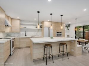 South Loop, Chicago, IL - Kitchen Remodel 3 Modern kitchen remodel in South Loop, Chicago featuring natural wood grain cabinets, a large waterfall island with marble-look countertops, open shelving, and pendant lighting. The design blends sleek finishes with warm textures for a contemporary urban look.