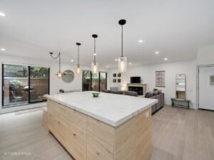South Loop, Chicago, IL - Kitchen Remodel 2 Wide view of a South Loop kitchen remodel with an open-concept layout flowing into the living room. Features include a large center island, pendant lighting, light wood cabinetry, and seamless connection to the family room and outdoor patio.